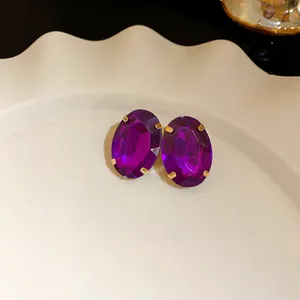 Close-up view of elegant purple oval faceted crystal stud earrings with gold prongs.