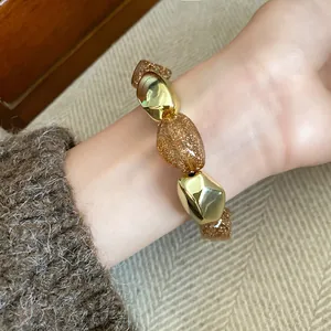 Dettaglio di un bracciale elastico in acrilico con perle dorate e ambra glitterate