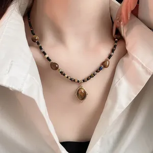 Detailed close-up of a vintage round tiger eye stone necklace worn with a white shirt