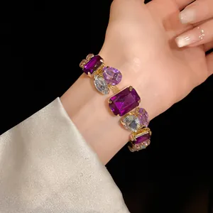 Close-up of a luxurious gold bracelet with large purple and blue faceted gemstones.