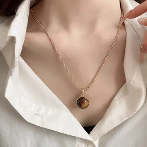Close-up of a vintage round tiger eye stone pendant on a gold twist rope chain necklace.
