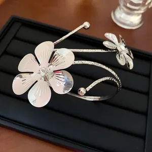 Primo piano di bracciale rigido aperto con fiori argentati e strass su vassoio