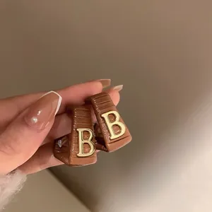Détail des boucles d'oreilles vintage en cuir marron avec un logo doré en forme de B