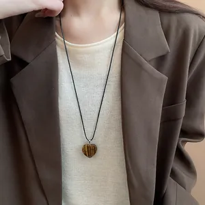 Close-up detail of a vintage heart-shaped tiger eye stone pendant necklace worn by model