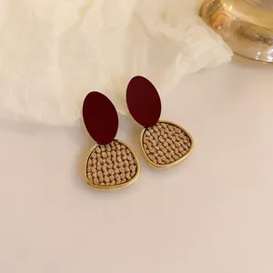 Close-up of elegant burgundy oval earrings with textured golden geometric pendants