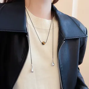 Close-up of a retro tiger eye stone sweater chain on a model wearing a leather jacket