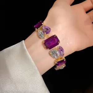 Close-up of a luxurious gold bracelet featuring large purple and clear faceted crystals.