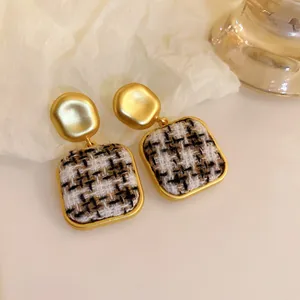 Close-up of vintage gold earrings with tweed fabric inlay in brown and black.