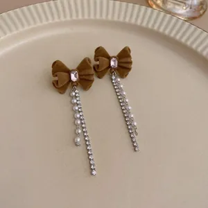 Détail des boucles d'oreilles nœud en velours marron avec longs pompons de strass et perles.
