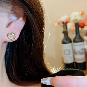 Detailed view of gold heart stud earring with pavé-set clear zircons on model's ear