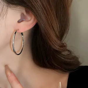 Close-up of a stylish minimalist silver metal hoop earring worn on a female model's ear.