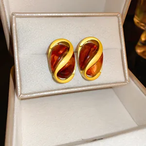 Gros plan de boucles d'oreilles vintage marron au design en spirale dorée dans un écrin de bijoux.