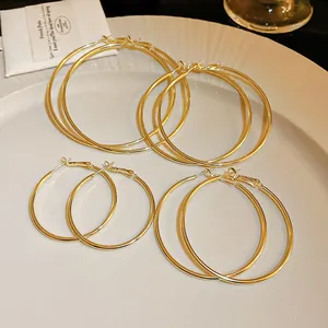 Detail view of four pairs of gold metal hoop earrings in various sizes on a white plate.