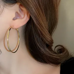 Detail view of a model wearing large minimalist gold hoop earrings with a high-shine finish.