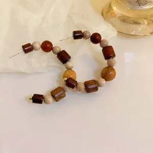 Close-up detail of handcrafted C-shaped hoop earrings with mixed wooden beads.