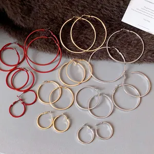 Collection of minimalist round hoop earrings in various sizes and colors on a textured background.