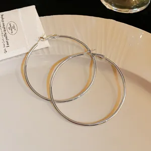 Detail shot of large minimalist silver hoop earrings on a textured plate background.