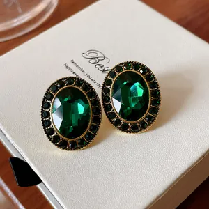Nahaufnahme von Vintage smaragdgrünen ovalen Ohrsteckern auf einer weißen Geschenkbox.