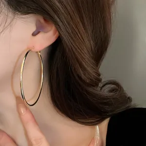 Close-up detail of large minimalist gold hoop earrings worn on a model with long wavy hair.