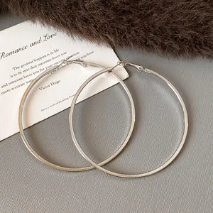 Detailed view of large silver-colored steel hoop earrings on a textured background.