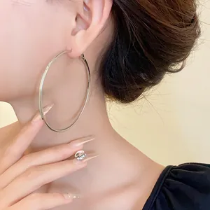 Detail shot of a large minimalist silver hoop earring worn on a female model's ear.