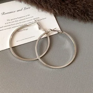 Close-up detail of large minimalist silver hoop earrings on a decorative prop card