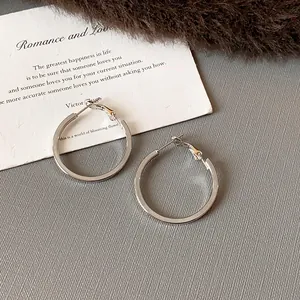 Close-up of minimalist silver round hoop earrings on a textured background with a quote card.