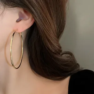 Detailed close-up showing a large gold-tone minimalist hoop earring worn by a model