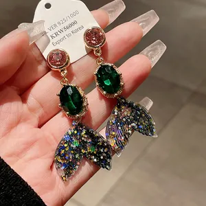 Close-up detail of mermaid tail drop earrings with vibrant glitter and green gems.