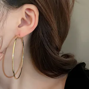Detail view of a large minimalist gold-tone circular hoop earring worn by a female model