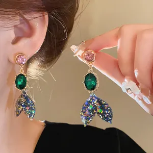 Close-up of elegant silver needle mermaid tail earrings with colorful green rhinestones