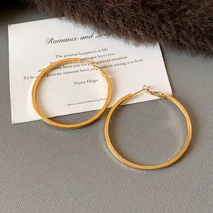 Macro view of gold-colored minimalist hoop earrings on a textured grey background
