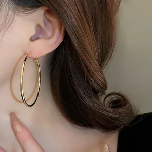High-quality close-up detail of minimalist large gold-tone hoop earrings worn by a model
