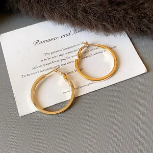 Detail view of stylish gold minimalist hoop earrings on decorative white card backdrop