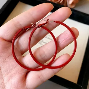 Detailed close-up showing vibrant red minimalist large hoop earrings held by a hand