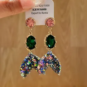 Detailed macro view of colorful crystal mermaid tail drop earrings with glitter finish
