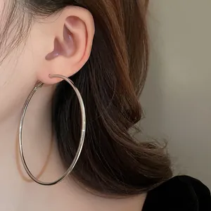 Close-up of a model wearing large silver metal hoop earrings with a minimalist design