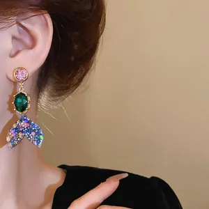 Macro shot of colorful rhinestone fishtail drop earrings worn by an Asian model.