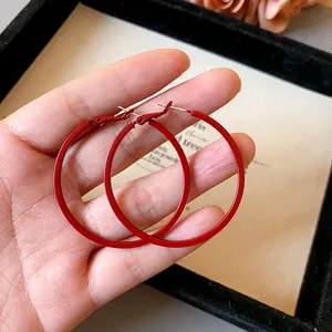 Detail view of large red minimalist round hoop earrings held by hand for size reference