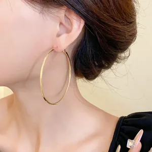 Detailed view of a large polished gold hoop earring worn by a model in minimalist style