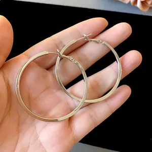 Macro view of large polished silver hoop earrings held in hand for scale