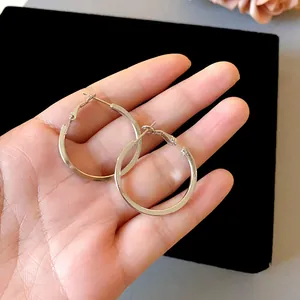 Macro detail view of minimalist silver stainless steel hoop earrings held by hand.