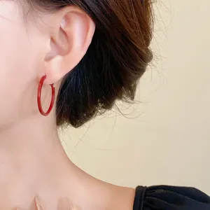 Detail view of red minimalist round hoop earrings with stainless steel pins on model