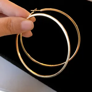 Detailed close-up view of large minimalist polished gold hoop earrings held by a hand