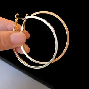 Detail shot of large minimalist gold-tone hoop earrings being held against a black background