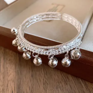 Close-up of silver-tone open bangle bracelet with dangling bell charms and textured pattern.