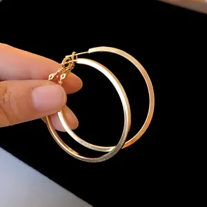 Detail of large gold-tone hoop earrings held by a hand on a black background