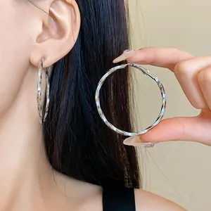 Dettaglio di grandi orecchini a cerchio attorcigliati color argento con elegante trama in metallo