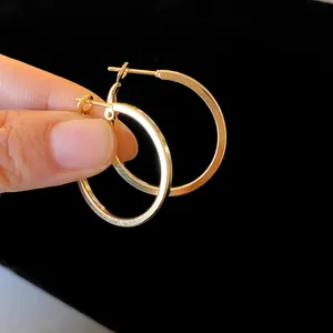 Close-up detail of large gold minimalist hoop earrings held by fingers on black background