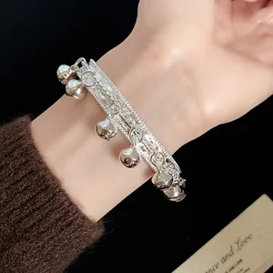 Silver ethnic style bracelet with textured band and dangling bell charms.